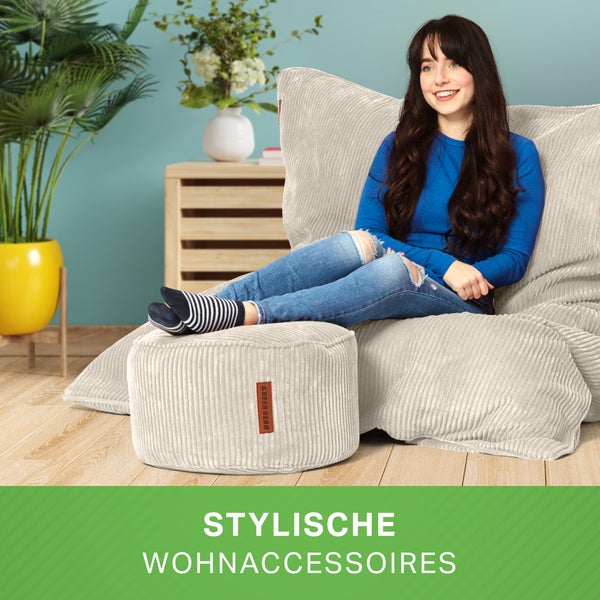 Frau sitzt entspannt auf einem Cord-Sitzsack mit passendem Hocker im Wohnzimmer.