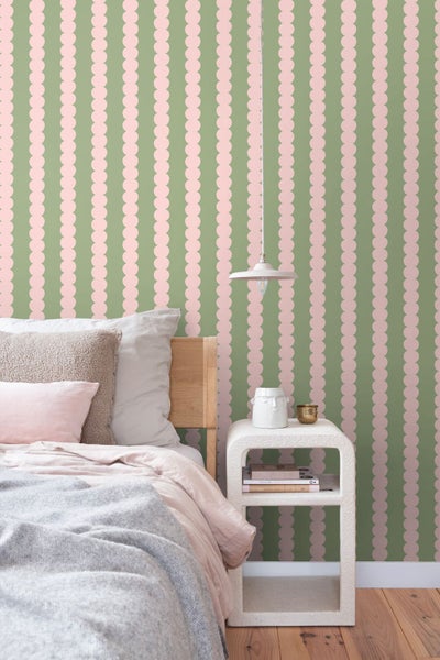 Schlafzimmer mit rosa-grüner Vliestapete mit vertikalem Muster aus Kreisen. Hell eingerichteter Raum mit Bett, Nachttisch und Pendelleuchte.