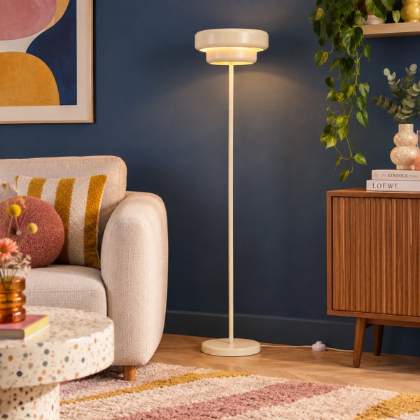 Moderne Stehlampe mit zweistufigem Schirm in einem wohnlich eingerichteten Wohnzimmer neben einem Sofa und einem Sideboard.