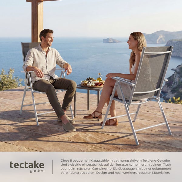 Zwei Personen sitzen in Garten-Klappstühlen aus Textilene auf einer Terrasse mit Meerblick. tectake garden Logo.