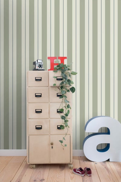 Gestreifte Tapete in Salbeigrün und Creme in einem hellen Zimmer mit Vintage Kommode, Pflanze und Holzboden.