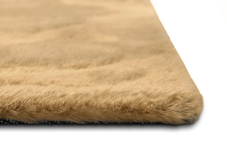 Nahaufnahme eines weichen beige Kunstfellteppichs mit hohem Flor und abgerundeter Ecke.