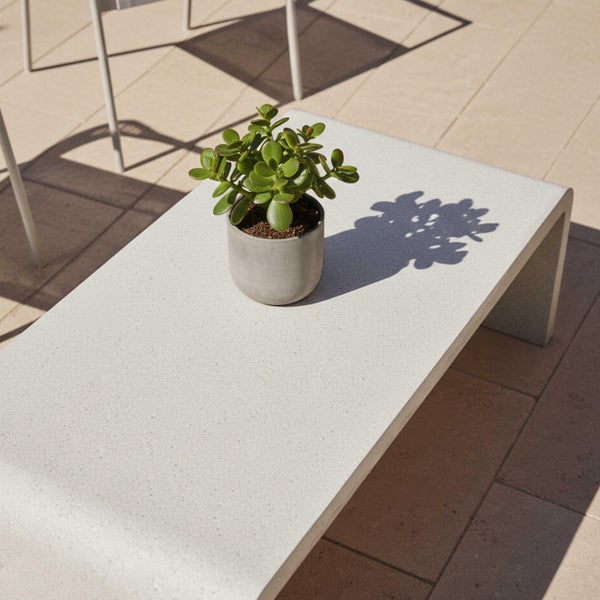 Moderner U-förmiger Garten-Couchtisch in Steinoptik mit einer kleinen Topfpflanze auf einer gefliesten Terrasse.