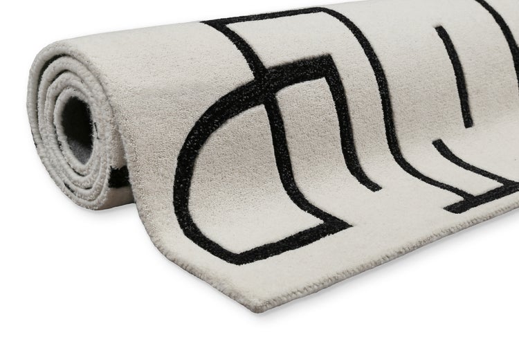 Zusammengerollter weicher Teppich mit schwarzem geometrischem Muster.