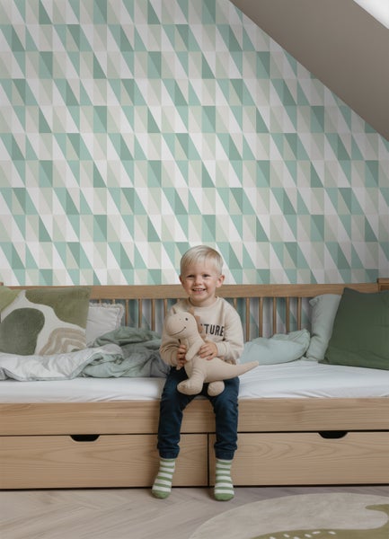 Kinderzimmer mit Holzbett und Tapete mit geometrischem Dreiecksmuster in Grün- und Weißtönen. Ein Kind sitzt auf dem Bett.