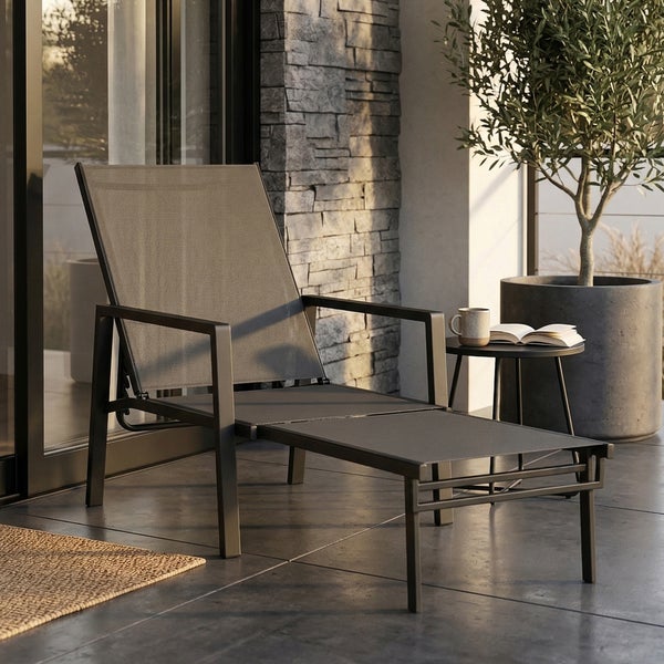 Moderne Gartenliege mit Armlehnen und Fußstütze auf einer Terrasse mit Natursteinwand, Beistelltisch und Olivenbaum im Topf.