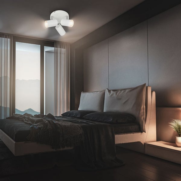 Moderner Deckenspot mit drei verstellbaren Leuchten in einem Schlafzimmer mit großem Bett und Wandpaneelen.