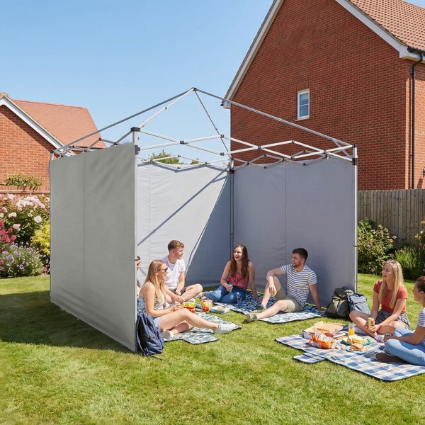 Faltpavillon-Gestell mit Seitenwänden auf einer Rasenfläche im Garten, eine Gruppe junger Leute macht ein Picknick.