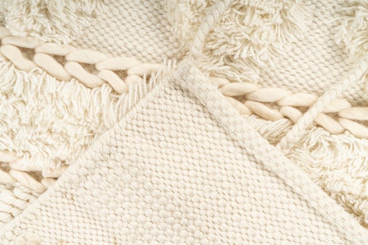 Nahaufnahme eines cremefarbenen Teppichs mit verschiedenen Texturen wie geflochtenen Elementen, Fransen und gewebter Oberfläche.