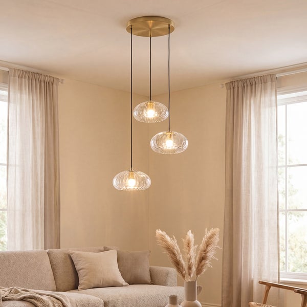 Moderne dreiflammige Pendelleuchte mit gerippten Glasschirmen über einem Sofa in einem hellen, wohnlichen Wohnzimmer.