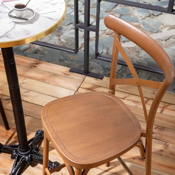 Bistrostuhl aus Metall in Holzoptik mit X-Rückenlehne auf einer Holzterrasse neben einem Tisch mit Marmorplatte.