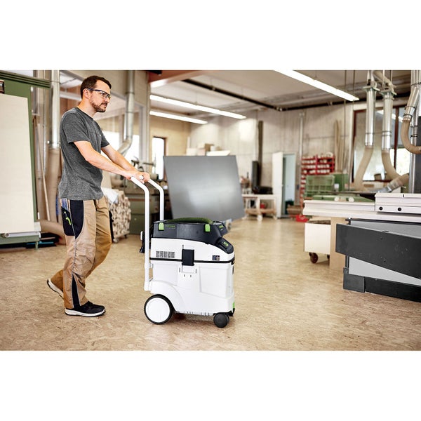 Ein Mann schiebt ein mobiles Festool Absaugmobil in einer hellen, organisierten Werkstatt mit Holzbearbeitungsmaschinen.