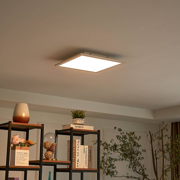 Modernes quadratisches LED-Panel Deckenleuchte in einem hellen Raum mit Metallregalen, Deko-Objekten und Zimmerpflanzen.