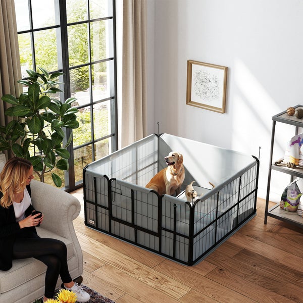 Quadratischer Welpenauslauf aus Metall und grauem Netzgewebe in einem hellen Wohnzimmer mit Parkettboden und Hunden.