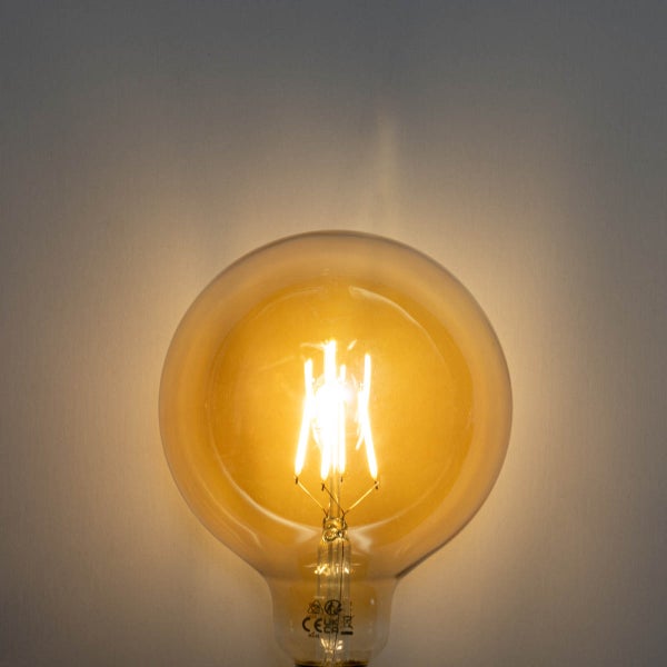 Eingeschaltetes LED-Filament-Leuchtmittel in Globusform mit bernsteinfarbenem Glas und warmweißem Licht.