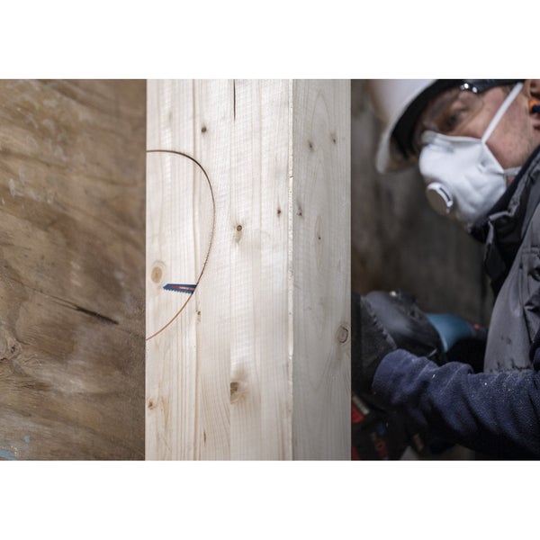 Mann mit Sicherheitsausrüstung sägt ein Loch in ein Holzbrett.