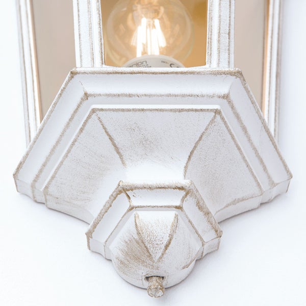 Nahaufnahme einer weißen Außenwandleuchte im Laternen-Stil mit Patina-Finish, Glasscheiben und leuchtendem Leuchtmittel.