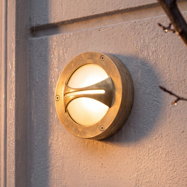 Runde Außenwandleuchte aus Messing mit warmem Licht und horizontaler Blende, an einer Wand montiert.