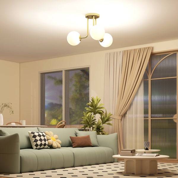 Moderne Deckenleuchte in Gold mit drei weißen Glaskugeln in einem hellen Wohnzimmer mit grünem Sofa und Teppich.