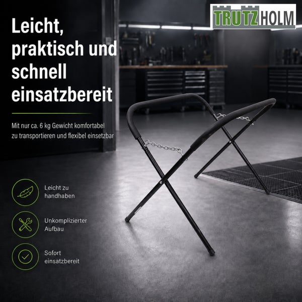 Schwarzer Trutzholm Montagebock aus Metall mit Polsterung und Sicherungsketten in einer Werkstatt. Trutzholm Logo. Wiegt circa 6 Kilogramm, einfacher Aufbau.