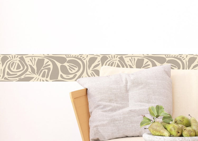 Selbstklebende Tapetenbordüre mit abstraktem floralem Muster in neutralen Erdtönen über einem Holzstuhl mit Kissen.