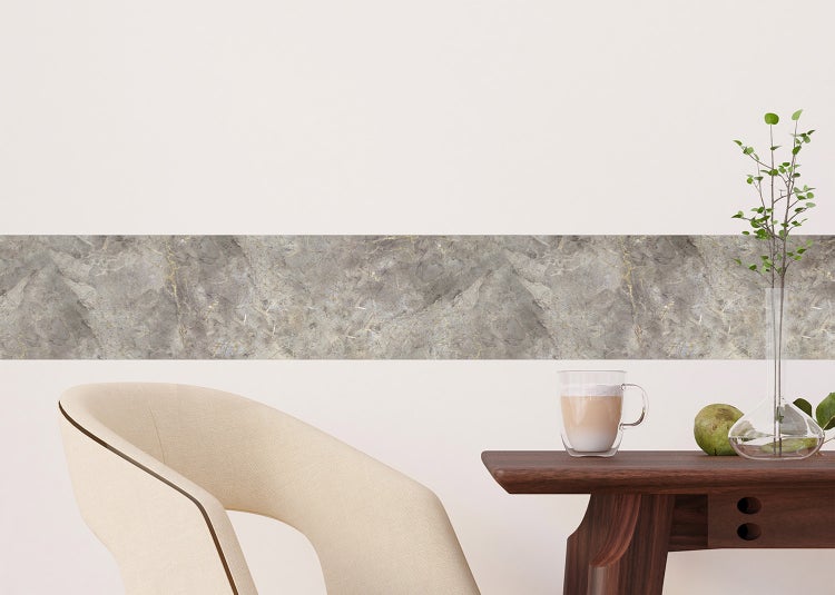 Selbstklebende Tapetenbordüre in Marmor-Optik an einer Wand in einem hellen, modernen Raum mit Tisch und Sessel.