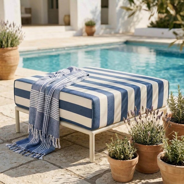 Gestreifter Gartenhocker mit Metallgestell an einem Pool, dekoriert mit einem Tuch und umgeben von Tontöpfen mit Pflanzen.