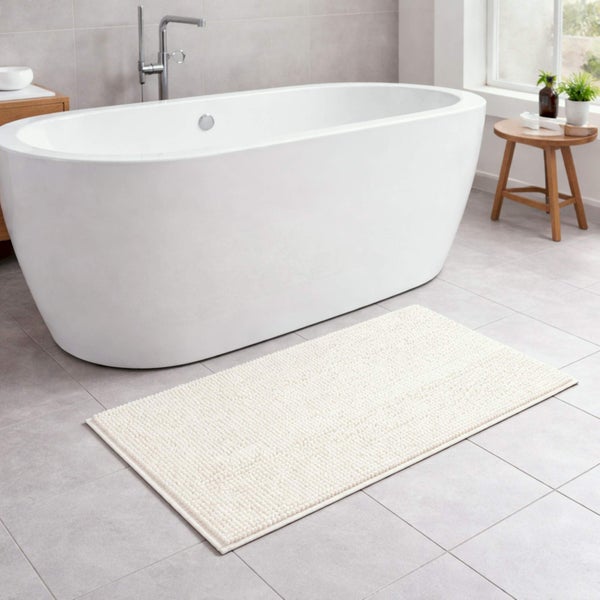 Badematte mit Noppenstruktur vor einer freistehenden weißen Badewanne in einem modern gefliesten Badezimmer.