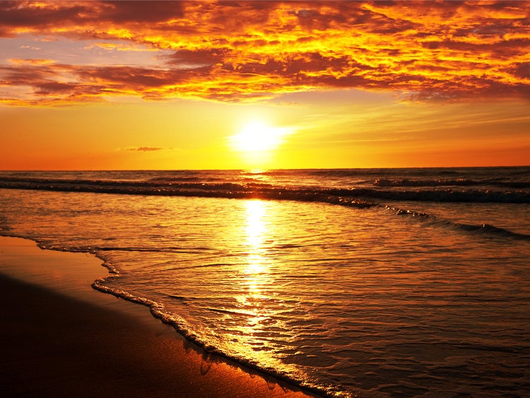 Sonnenaufgang über dem Meer mit Wellen und Sandstrand
