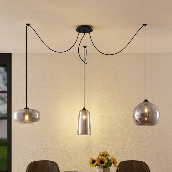 Dreiflammige Pendelleuchte im modernen Design mit schwarzen Kabeln und verschieden geformten Schirmen aus Rauchglas über einem Esstisch.