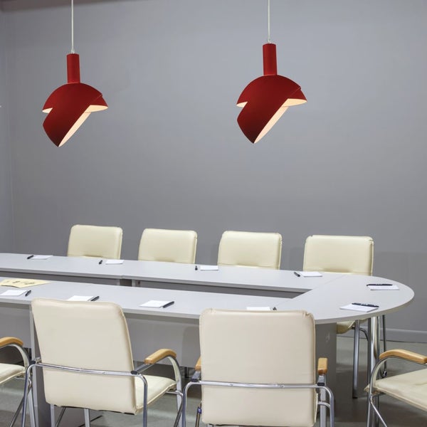 Konferenzraum mit ovalem Tisch, Bürostühlen und zwei roten Pendelleuchten