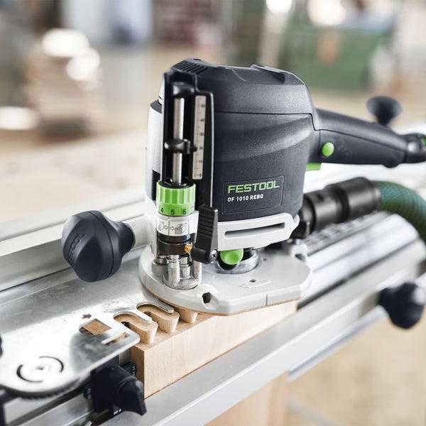 Festool Oberfräse OF 1010 REBQ beim Fräsen einer Holzverbindung auf einer Führungsschiene in einer hellen Werkstatt.