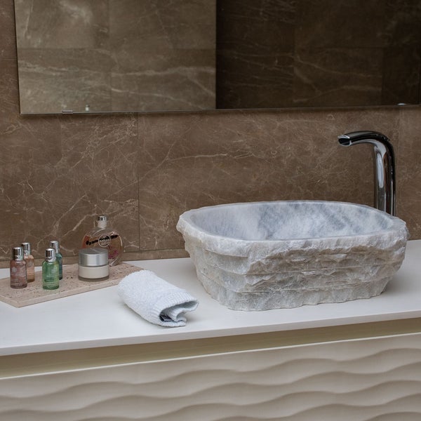 Modernes Badezimmer mit einem Aufsatzwaschbecken aus Naturstein auf einem weißen Waschtisch vor einer Wand in Marmoroptik.