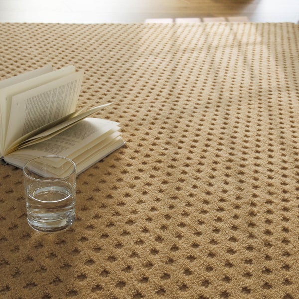 Beige strukturierter Teppichboden mit Rautenmuster, auf dem ein offenes Buch und ein Glas Wasser stehen.