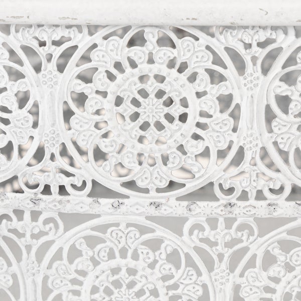 Detail eines weißen, filigranen Metallmusters mit verschnörkelten Ornamenten im Antik-Stil.