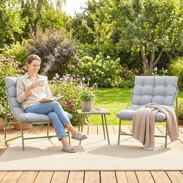 Zwei Garten Loungesessel mit grauen Polstern und grünem Metallgestell sowie ein kleiner Beistelltisch auf einer hellen Terrasse.