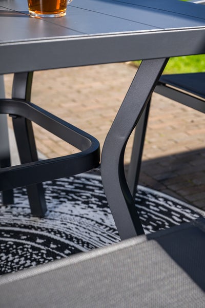Detailansicht eines schwarzen Gartentischs und Stuhls aus Aluminium mit geschwungenen Beinen auf einer Terrasse.