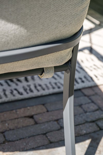 Detailansicht eines Gartenstuhls mit Sitzkissen aus Stoff, das mit einer gewebten Schlaufe am Metallrahmen befestigt ist.