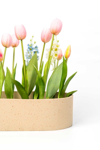 Künstliche Tulpen und Feldblumen in einer ovalen, gesprenkelten Pflanzschale.