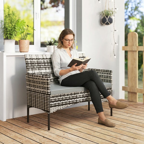 Frau liest auf einer Zweisitzer Gartenbank aus Polyrattan mit Sitzkissen auf einer Terrasse mit Holzboden und Pflanzen.