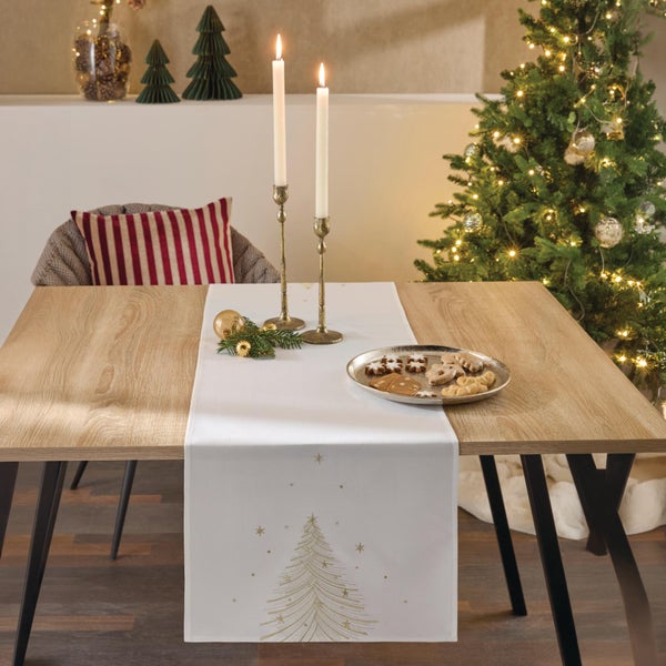 Festlich gedeckter Esstisch mit weihnachtlichem Tischläufer, der mit Tannenbaum Stickerei verziert ist, Kerzenleuchtern und Plätzchenteller.