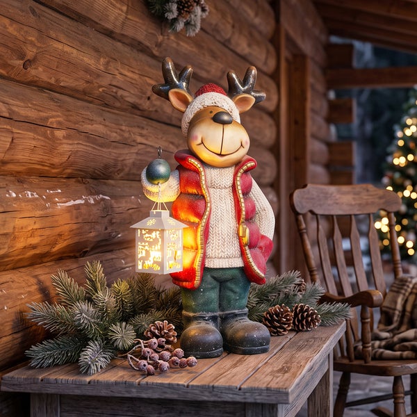 Dekorative Rentierfigur mit LED Laterne für die Weihnachtsdekoration auf einem Holztisch vor einer Blockhauswand.