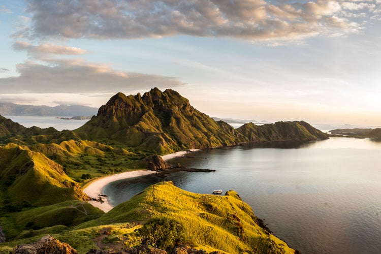Weitwinkelansicht der Insel Padar im Komodo Nationalpark in Indonesien mit einer Bucht und bewachsenen Hügeln bei Sonnenaufgang