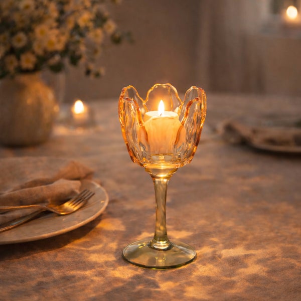 Gläserner Teelichthalter in Tulpenform mit hohem Stiel auf einem gedeckten Tisch mit brennendem Teelicht.