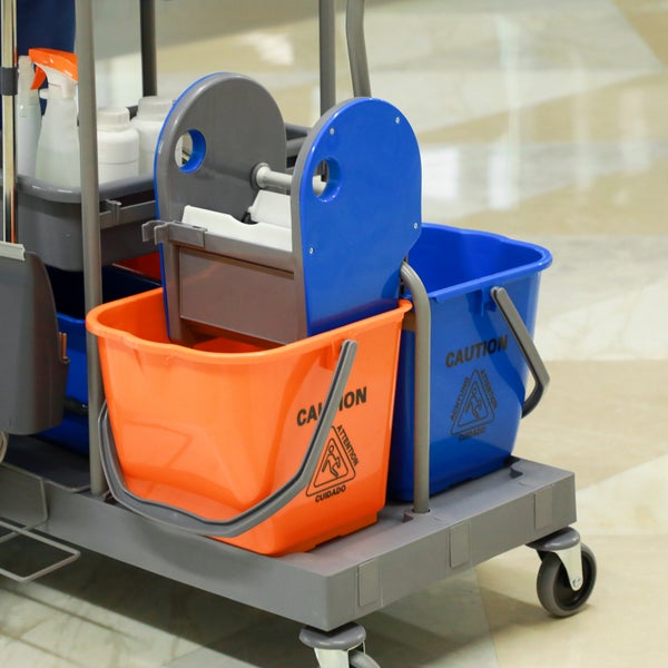 Fahrbarer Reinigungswagen mit zwei Eimern mit Warnhinweisen, einer Wringvorrichtung und Reinigungsmitteln auf einem stabilen Gestell mit Rollen.