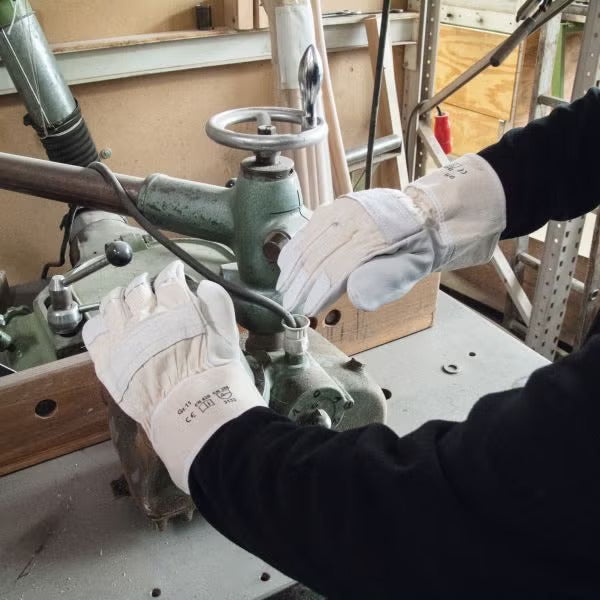 Person bei der Arbeit an einer Werkzeugmaschine, trägt robuste Schutzhandschuhe aus Leder für sicheres Arbeiten in der Werkstatt.