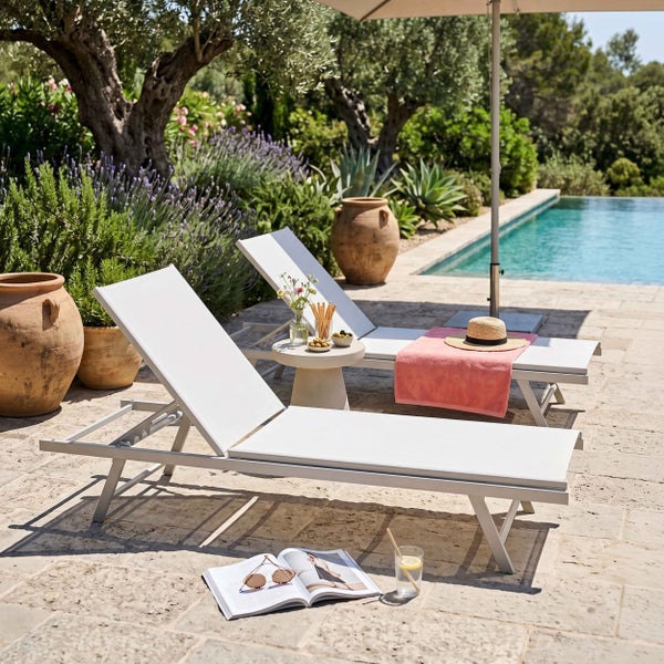 Zwei moderne Gartenliegen auf einer Steinterrasse am Pool, umgeben von einem mediterranen Garten mit Lavendel und Olivenbäumen.