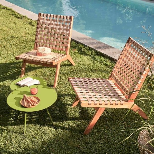 Zwei Garten-Lounge-Sessel aus Holz mit Geflecht und ein grüner Metalltisch auf einer Rasenfläche neben einem Pool.