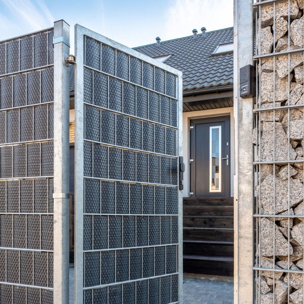 Einfahrtstor aus Metall mit Gabionenwand vor einem Wohnhaus