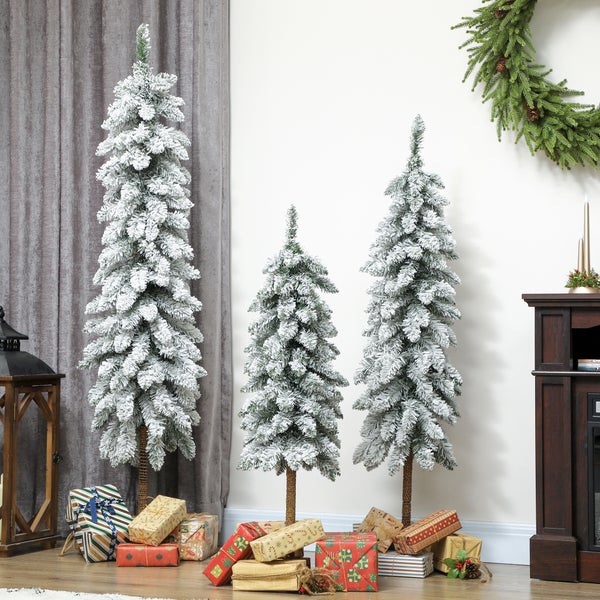 Drei verschieden hohe, schmale künstliche Weihnachtsbäume mit Kunstschnee und zahlreichen Geschenken in einer weihnachtlichen Raumszene.